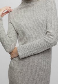 Pull à col roulé gris clair avec des côtes et des manches longues. Caractéristiques d'un tissu texturé avec un design ajusté, mettant en valeur la silhouette.
