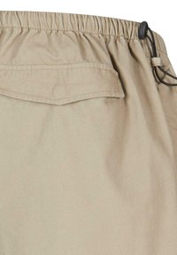 Shorts beiges avec taille élastique et cordon de serrage. Comprend une poche arrière avec rabat et une texture de tissu lisse.