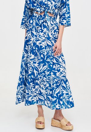 Maxi-Rock in Blau und Weiß mit floralem Muster, gestuftem Design und elastischem Bund. Kombiniert mit Wedge-Sandalen mit geflochtenen Akzenten.