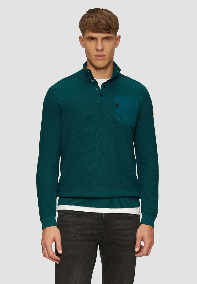 Türkisfarbener Strickpullover mit Kragen und Knopfverschluss, der eine Kontrasttasche aufweist. Die Textur wirkt weich, mit gerippten Bündchen und Saum.