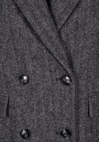 Dvoubarevný blejzr s šedým herringbone vzorem, vybavený černými knoflíky, zářezovými klopami a bočními kapsami s texturovaným povrchem.