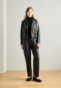 Black leather biker jacket with silver hardware, paired with loose black leather pants and chunky black platform shoes. Smooth texture and fitted design.