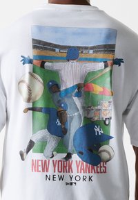 Camiseta blanca con un gráfico colorido de jugadores de béisbol, una pelota de béisbol y un carrito de vendedor, con el texto "NEW YORK YANKEES".