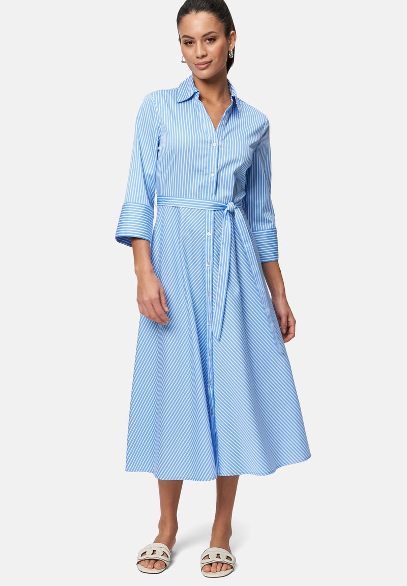 Blau-weiß gestreiftes Hemdkleid, knielang, mit kurzen Ärmeln und durchgehender Knopfleiste, mit gebundenem Taillengürtel, kombiniert mit weißen Sandalen.