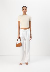 Top corto beige a coste, pantaloni bianchi a gamba larga con vita elasticizzata e una piccola borsa marrone con manici corti. Sandali con tacco trasparente.