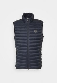 Gilet imbottito blu navy con colletto alto, zip frontale e tasche laterali. Presenta un'emblema del logo sul petto. Materiale liscio e leggero.