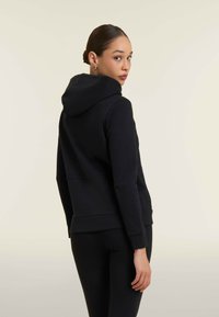 Sweatshirt à capuche noir avec une coupe décontractée, texture lisse et poignets côtelés, vu de dos avec un design minimaliste.