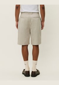 Lyse beige shorts med rett snitt, med to baklommer. Brukt med kremfargede sokker og brune sko. Vist bakfra.