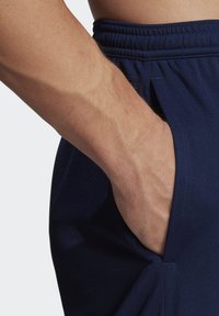 Shorts de sport navy avec une taille élastique et des poches latérales, montrant une main reposant dans la poche, fabriqués dans un tissu lisse.
