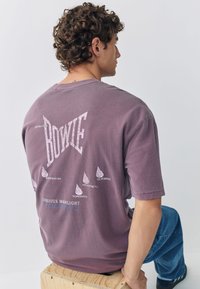 Lila oversize t-shirt med "BOWIE"-grafik på baksidan, med stadnamn. Mjuk textur, korta ärmar och rund halsringning.