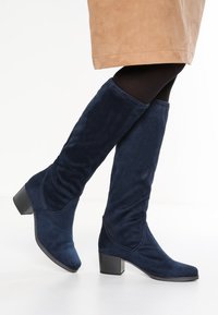 Navy blue suede knee-high boots with a chunky heel, featuring a sleek, smooth design and slight gathering at the shaft for added texture.