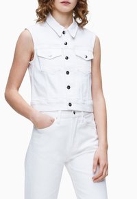 Weißes Denim-Cropped-Westen mit Kragen, Vorder pockets und schwarzen Knöpfen. Kombiniert mit passenden weißen, hoch taillierten Jeans. Glatte Textur.