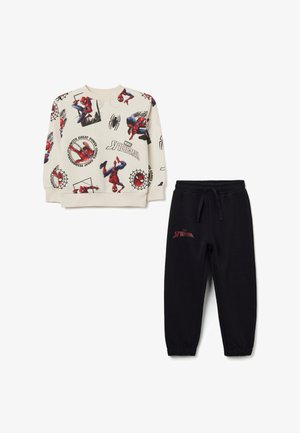 Sudadera crema con gráfico de Spider-Man, puños acanalados, combinada con pantalones jogger negros que presentan texto rojo de "Spider-Man" en el muslo.
