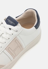 Weiße Ledersneaker mit beigen Wildledereinsätzen, navyfarbenem Fersenbereich und strukturiertem seitlichen Design, ausgestattet mit flachen Schnürsenkeln und einem gepolsterten Kragen.