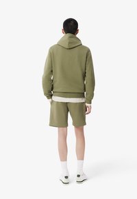 Sudadera verde oliva y pantalones cortos a juego, hechos de una tela suave, con puños acanalados y un diseño en capas con una camiseta interior de color claro.