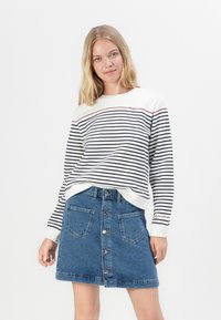 Gestreepte sweatshirt in roomkleur en marineblauw met rode accenten, gecombineerd met een blauwe denim blouserok met voorzakken en een getailleerd silhouet.