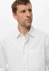 Camisa blanca de botones con finas rayas verticales, cuello clásico y un bolsillo en el pecho. El material parece suave y ligero.