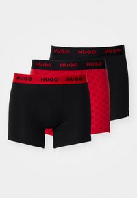 Three pairs of boxer shorts: two black with red waistbands, one red with a checkerboard pattern, all featuring HUGO branding.