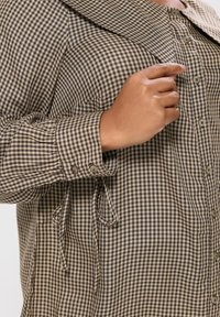 Camicia a quadri in marrone e beige, con colletto, maniche arrotolate con bottoni e dettagli legati in vita.