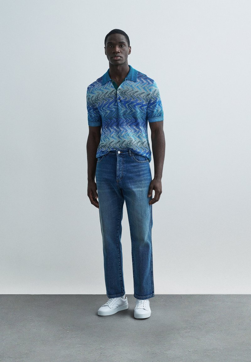 Polo bleu et vert à motifs avec col, associé à un jean droit bleu et des baskets blanches. Design simple, coupe décontractée.