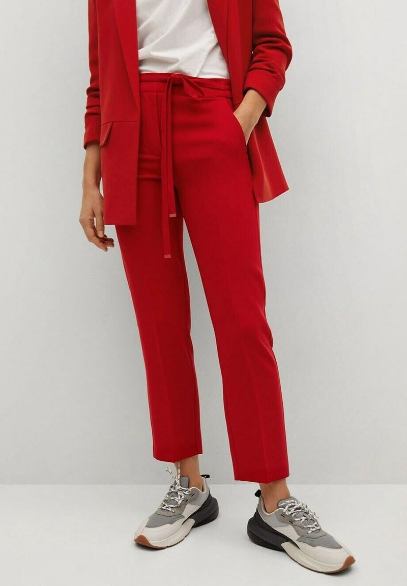 Pantalon rouge sur mesure avec taille à nouer, présentant une coupe slim et une longueur raccourcie, associé à des baskets grises et blanches.