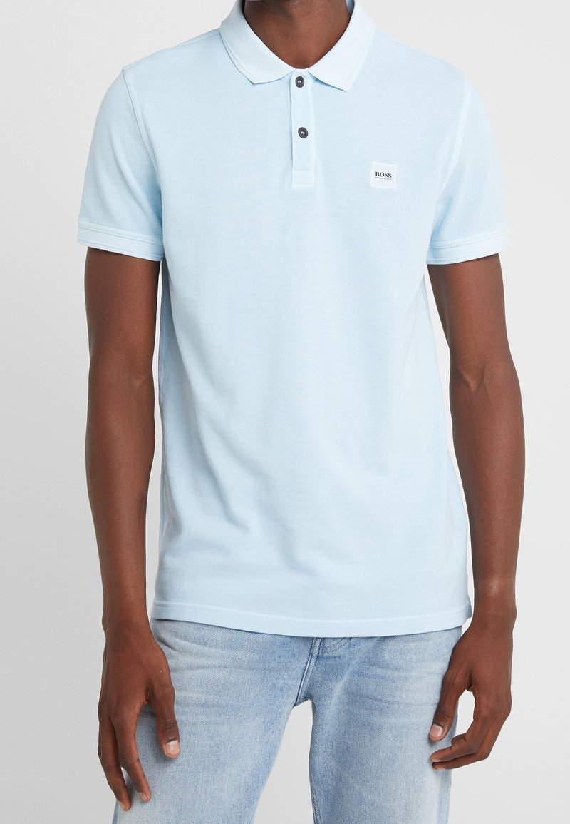 Světle modrá polo košile vyrobená z bavlny, s klasickým límečkem, dvouknoflíkovou légou s tmavými knoflíky a malou nášivkou s logem na prsou.