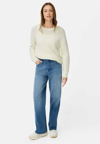 Lichtcrème gebreide trui met een losse pasvorm, lange mouwen en subtiele structuur; gecombineerd met relaxed-fit blauwe jeans en witte sneakers.