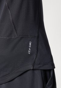 Nærbilde av svart sportsklær med synlig "DRI-FIT"-logo på teksturert, sydd stoffpanel.