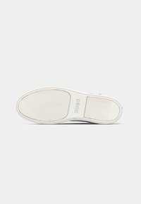 Semelle de chaussure blanche avec motifs antidérapants texturés et le mot « HUGO » embossé dans la zone de la voûte, présenté sur un fond uni.