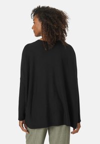 Zwarte oversized trui met een losse pasvorm, geribbelde textuur en verlaagde schouders. Heeft lange mouwen en een ronde halslijn.