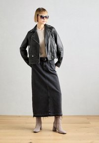 Černá kožená motorkářská bunda, krémový top, dlouhá černá džínová sukně a šedé kotníkové boty se čtvercovými podpatky. Celý vzhled doplňují velké tmavé sluneční brýle.