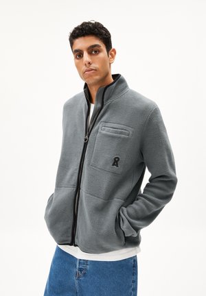 Gray fleece jacket with a high collar, front zipper, chest pocket, and logo accent. Features a relaxed fit and side pockets.