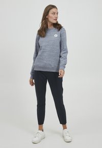 Grå genser med rund hals, med en liten logo på brystet. Kombinert med marineblå smale bukser og hvite joggesko.