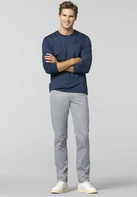 Marineblaues Langarmhemd aus strukturiertem Stoff, kombiniert mit hellgrauen Slim-Fit-Hosen und weißen Sneakers, die Arme in einer neutralen Pose verschränkt.