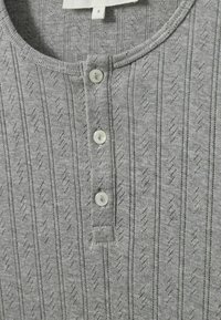 Siva henley majica sa teksturiranim uzorkom i vertikalnim prugama, tri dugmeta i rebrastim ovratnikom i rukavima.