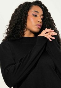 Zwarte gebreide trui met een hoge hals, lange mouwen en ribgebreide manchetten. Heeft een gladde textuur en een aansluitend ontwerp.