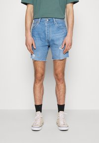 Light blue denim shorts with distressed details, frayed hem, and a five-pocket style. Paired with beige high-top sneakers and black socks.