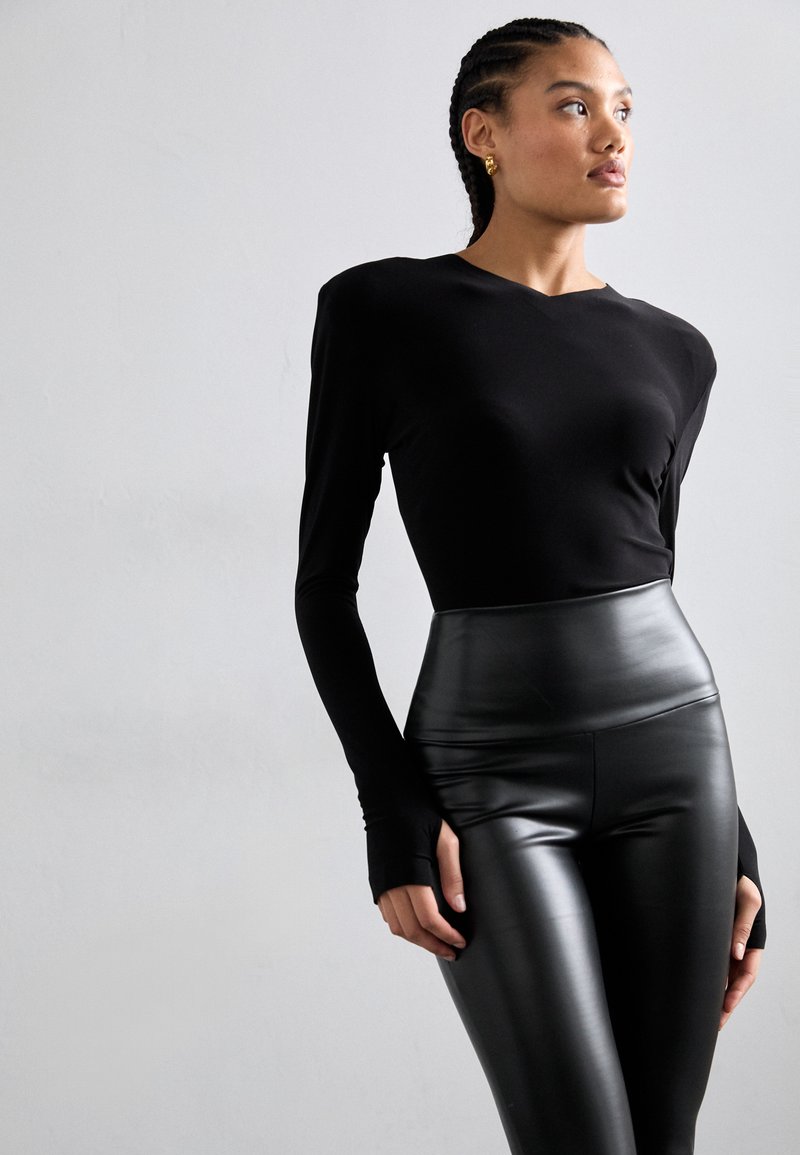 Schwarzes langärmliges Oberteil mit taillierter Passform, kombiniert mit hochtaillierten schwarzen Leggings aus Kunstleder mit glatter Textur und schlankem Look.
