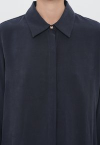 Camisa de manga larga azul marino hecha de una tela suave y lisa, con un cuello clásico y un cierre de botón en el cuello.