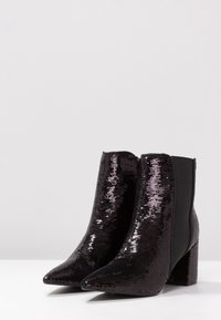 Stivali neri alla caviglia con punta affilata, ricoperti di paillettes. Tacco quadrato spesso e pannelli laterali elastici per una facile calzata. Fodera interna liscia.