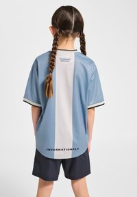 Ljusblå sporttröja med vit vertikal rand, svart krage och ärmar. Har "INTERNATIONALS" tryckt nära fållen och logotyp på baksidan.