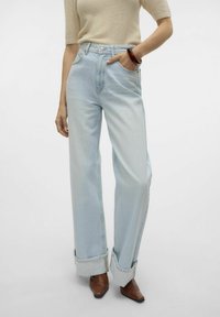 Šviesiai mėlynos, aukštu juosmeniu, laisvos formos džinsai, su apvyniotais rankogalviais ir priekinėmis kišenėmis. Džinsinio audinio tekstūra su minimaliu siuvimo detalių.