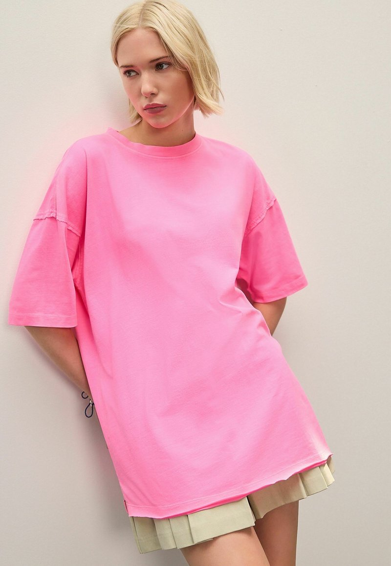Overmaat roze katoenen t-shirt met korte mouwen, ronde halslijn en een soepele textuur, gecombineerd met een geplooide beige rok.