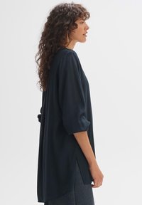 Schwarze, leichte Bluse mit lockerem Schnitt, dreiviertellangen Ärmeln, seitlichen Schlitzen und glatter Textur. Geeignet für legere oder geschichtete Outfits.