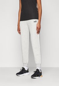 Pantalons de sport en coton gris avec des poignets côtelés et un petit logo Puma noir. Associés à des chaussures de sport noires et des chaussettes blanches. Design simple dans l'ensemble.