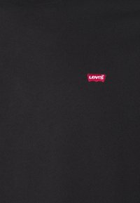 Černé bavlněné tričko s kulatým výstřihem a malou červenou nášivkou loga Levi's na levé části hrudi. Měkká textura, jednoduchý design.