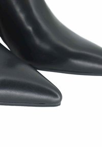 Zapatos de tacón alto negros con diseño de punta afilada, fabricados en cuero liso con textura mate y suela exterior sólida negra.