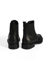 Bottines Chelsea en cuir noir avec des panneaux latéraux en élastique, des orteils ronds et des tirettes, présentant une finition texturée et des talons bas.