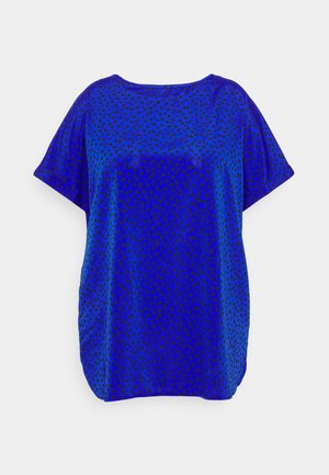 Blouse bleue à manches courtes, coupe ample avec motif intégral de petits pois noirs sur fond blanc.