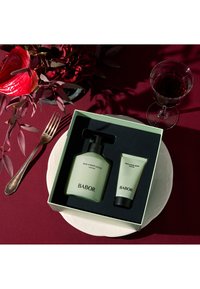 Babor soul en body lotion in een matte groene fles met pomp en een bijpassende tube douchegel, beide in een zwarte doos op een bord.